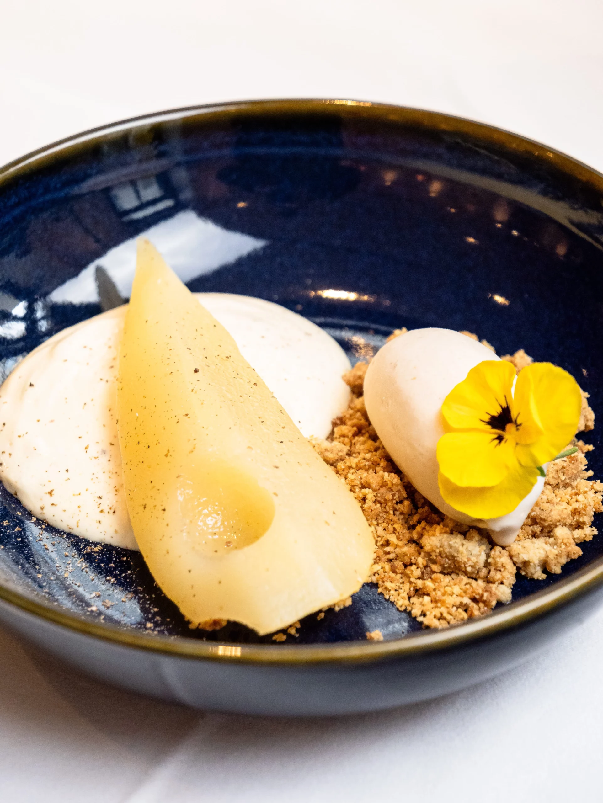 Photo d'une assiette dessert, contenant de la poire pochée, un crumble, une glace, et une espuma